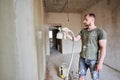 Builder is painting with airbrush wall, house repairment. Large volume of work is visible in the background