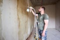 Builder is painting with airbrush wall, house repairment. Large volume of work is visible in the background