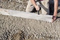 Builder placing edging pin kerb on semi-dry concrete using a string line to keep them straight during construction of footpath