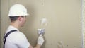 The builder plasters the wall in the room. A man in special clothes and a helmet makes repairs.