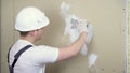 The builder plasters the wall in the room. A man in special clothes and a helmet makes repairs.