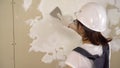 The builder plasters the wall in the room. A woman in special clothes and a helmet makes repairs.