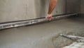 A builder in protective gloves pours a self-levelling screed onto the floor and applies a liquid cement mortar with a