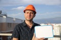 Builder in a protective helmet with a tablet for writing in his hand is standing on the roof of a building overlooking the city Royalty Free Stock Photo