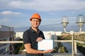 Builder in a protective helmet with a tablet for writing in his hand is standing on the roof of a building overlooking the city Royalty Free Stock Photo