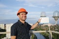 Builder in a protective helmet with a tablet for writing in his hand is standing on the roof of a building overlooking the city Royalty Free Stock Photo