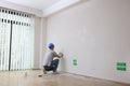 A male builder plasters a white wall in a room