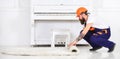 Builder removing carpet. Side view guy in blue overall and orange helmet in front of white piano. Home redesign