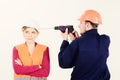 Builder, repairman makes hole in female head. Woman with bored face in helmet ignoring husband annoying her.