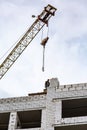 Builder on the roof of a white brick house under construction and a crane against the sky. Vertical orientation. Royalty Free Stock Photo