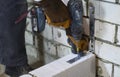 Builder screwing joining clamp in aerated concrete block with electric drill