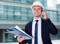 Builder in suit and hat with folder is taking folder and discussing projec by the phone