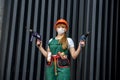 Builder with tools. Woman in green coverall and protective mask holding drill machine on abstract background