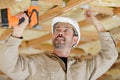 Builder using cordless drill on wooden ceiling joists