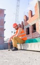 Builder vest and helmet construction site sit relaxing. Guy protective helmet sit in front of building made out of Royalty Free Stock Photo