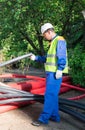 Builder, in a white helmet and a yellow vest, checks black pipes for laying electric cables under city lighting Royalty Free Stock Photo