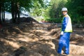 Builder, in a white helmet and a yellow vest, stands on the background of excavated soil, before preparing for the landscape