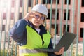 Builder woman on construction site in green vest and white helmet with tablet. A middle-aged woman looks at the camera. She writes Royalty Free Stock Photo