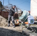 Builder works with concrete mixer. Construction worker with shovel in hand