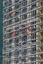 Builders team in red uniform work outdoors on scaffolding covering facade of new residential apartment building.