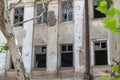 A building with broken windows and cracked walls, surrounded by trees in the city including an old white concrete structure Royalty Free Stock Photo
