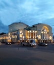 The building is in a classic style in the evening. The walls are painted yellow. Above the entrance - columns. Summer evening.