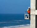 Building construction worker high over ocean beach