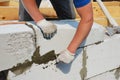 A building contractor is constructing a wall from autoclaved aerated concrete blocks using a trowel and an axe, attaching concrete