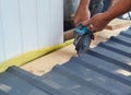 A building contractor is cutting lightweight metal, steel, corrugated, paint coated roofing sheet with an electric angle grinder