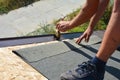 A building contractor is installing underlayment, a layer of bitumen tape on sheathing for overall roof protection at the ridge of
