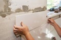 A building contractor is installing white rectangle large ceramic tiles on a wall next to the window renovating the bathroom Royalty Free Stock Photo