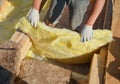 A building contractor is laying mineral wool sheets in protective gloves on the rooftop for thermal insulation, energy efficiency