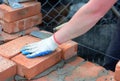 A building contractor in protective gloves is laying bricks using a mason`s line, spade trowel and mortar to construct a wall of Royalty Free Stock Photo