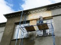 A building contractor on scaffolding is plastering, applying stucco finish, rendering a roof soffit and the exterior wall of an Royalty Free Stock Photo