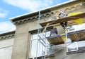 Building contractors on scaffolding near rooftop are rendering, plastering, stucco coating the exterior wall of the building using Royalty Free Stock Photo