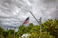 Building crane used to fly giant American flag about roofs and treetops with downtown skyscraper in distance - cloudy dramatic sky