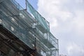 Building facade under renovation works with construction scaffolding frame covered with protective net for workers Royalty Free Stock Photo