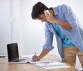 Building his client network. Handsome young ethnic businessman writing something down while speaking on the phone. Royalty Free Stock Photo