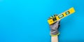 Building level. Hand in gloves holds a yellow building level on a blue background. Postcard or poster for print, place Royalty Free Stock Photo