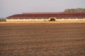 The building of a livestock farm and a plowed field during sunset. An agricultural field on the territory of an industrial complex Royalty Free Stock Photo