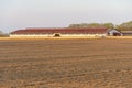 The building of a livestock farm and a plowed field during sunset. An agricultural field on the territory of an industrial complex Royalty Free Stock Photo