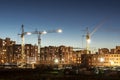 Building site with three tower cranes against the background of multi-storey houses and a blue sky, night scene Royalty Free Stock Photo