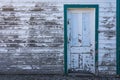 This old building has narrow wood slats with a wooden panel door. The colors are white and green & paint is worn away. Royalty Free Stock Photo