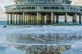 Building on stone weathered poles at the beach of scheveningen with waves in the sea and reflection in the wet sand Royalty Free Stock Photo