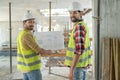 Building workers in yellow vests turning thier heads to camera, holding blueprint