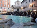 Buildings in the background, many tourist people in front of a historical monument with a fountain