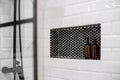 Built-in shelf with bottles in modern bathroom. Shower wall with white tiles. Royalty Free Stock Photo