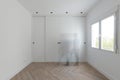 Built-in wardrobe with white wooden sliding doors in a room with aluminum windows and a ghost passing in front of the wardrobe