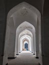 Bukhara, Uzbekistan, April 2018: Kalyan Mosque. A corridor of white arches, through which you can see a bench with a Muslim woman