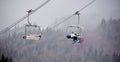 Bukovel, Ukraine - December 09, 2018: family skiers carrying up on cable chairlift over coniferous forest in dense fog